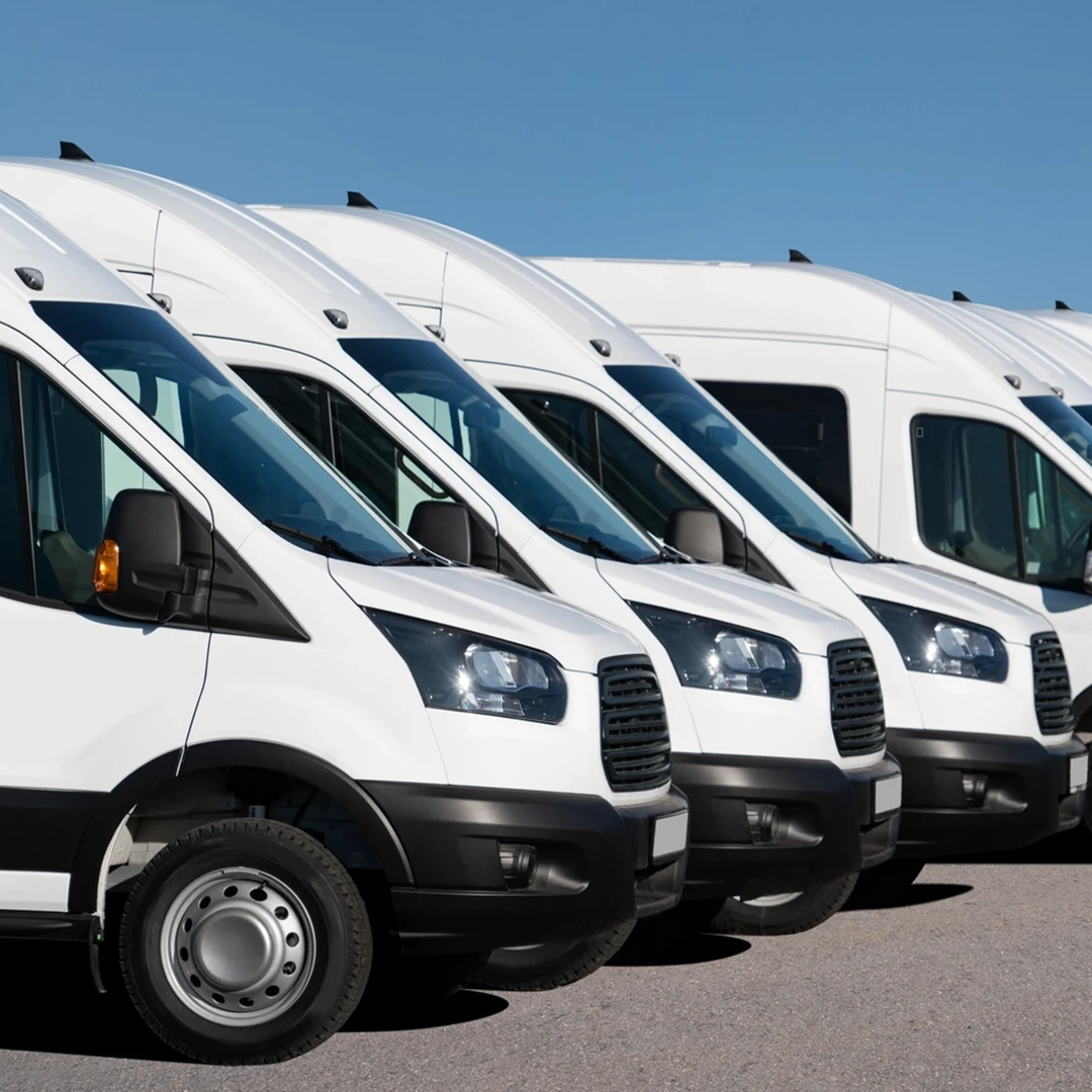 A row of white delivery vans lined up against a clear blue sky, showcasing their front profiles and wheels.